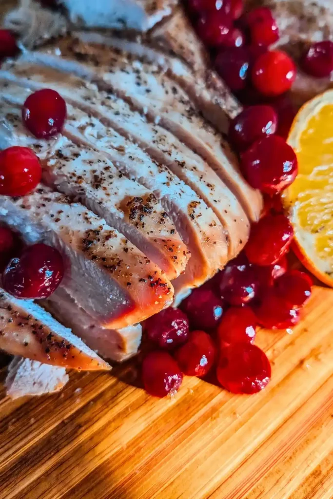 sliced baked turkey breast on wood cutting board with cranberry orange garnish