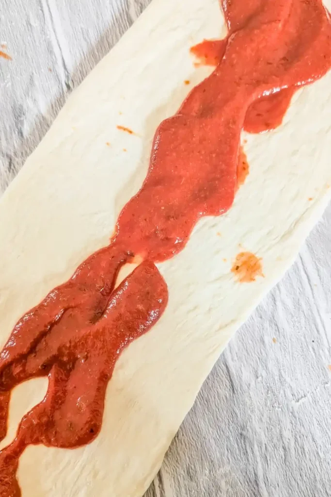 adding pizza sauce to the rolled pizza dough