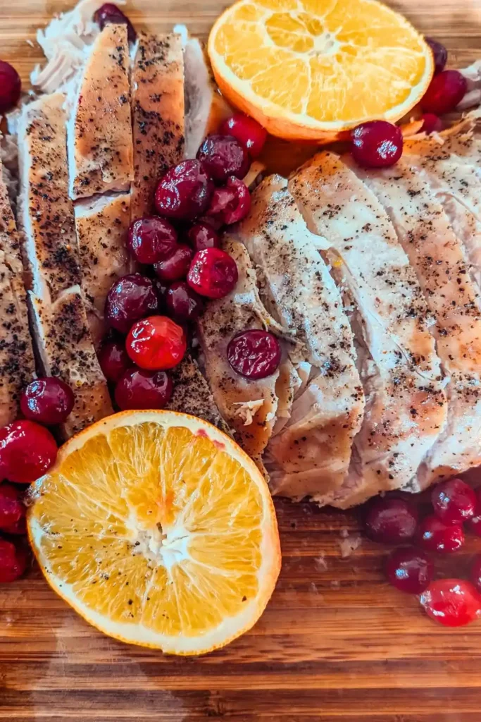two sliced turkey breast with salt and pepper seasoning and red cranberries and orange slices on wood cutting board