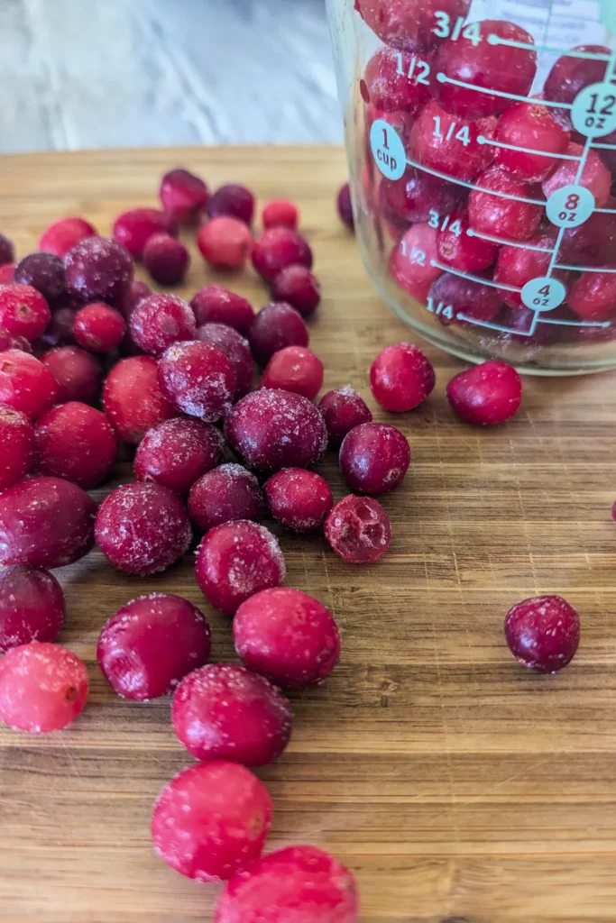 whole cranberries on cutting board a measuring cup with more frozen berries sits upper right