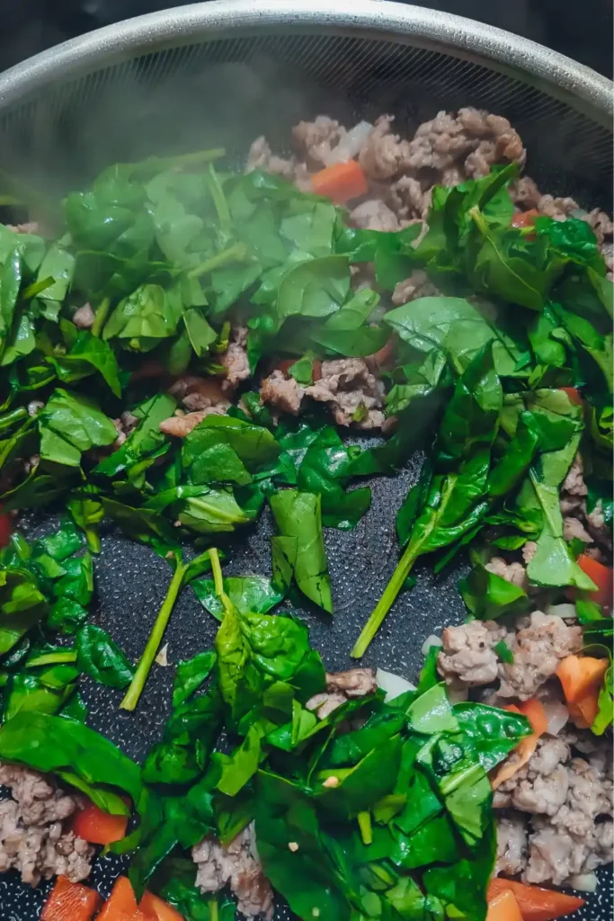 adding baby spinach to the frying pan