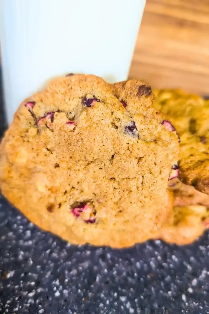 close up baked cranberry white chocolate chip cookie leaning against old timey milk bottle