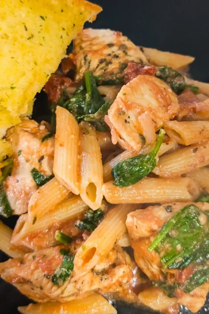 the rose sauced chicken penne pasta on black plate with a side of garlic bread