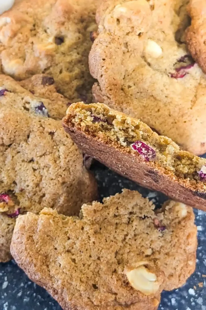a white chocolate cranberry cookie with cashews broken in half leaning on other cooling cookies