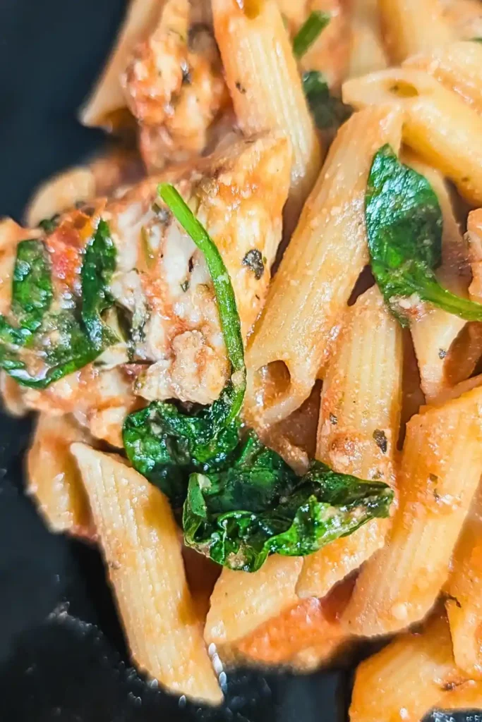 a large spinach leave sits on the rose sauced chicken pasta