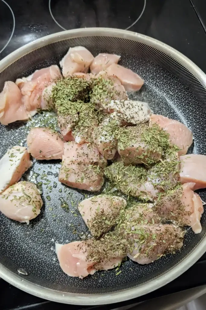 adding dry savory and basil to chicken breast pieces in frying pan