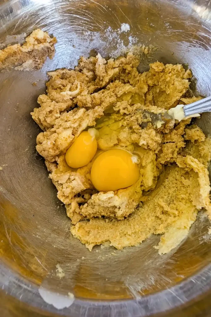 adding eggs to creamed butter mixture in stainless steel mixing bowl