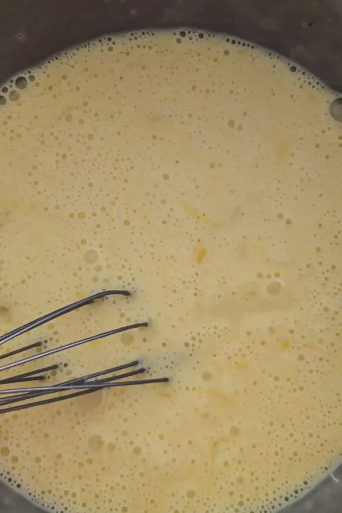 whisked eggs and cream in mixing bowl with whisk visible