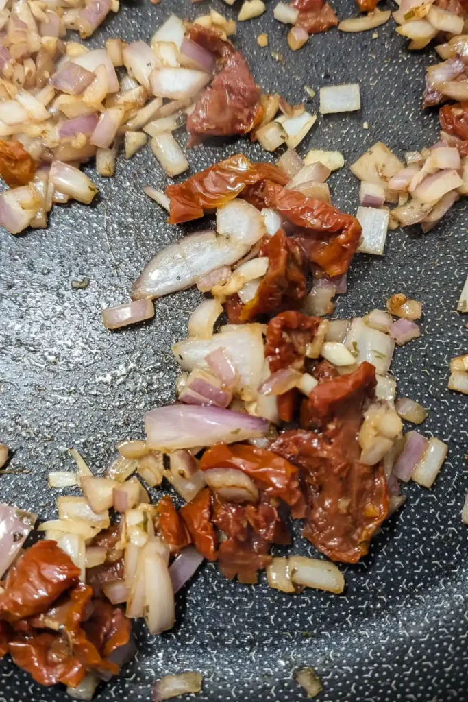 adding sun dried tomato to the onion and garlic in pan