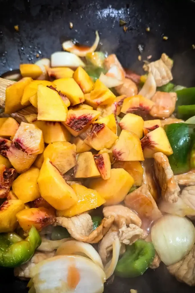 adding the fresh peaches to the pork stir fry