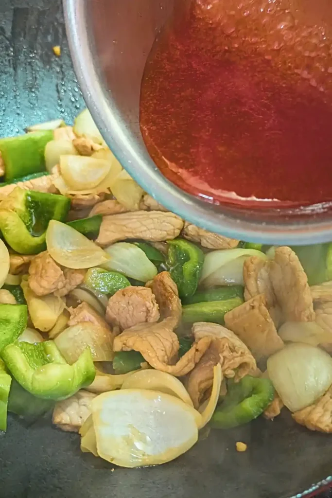 adding the sweet and sour sauce to the pork stir fry