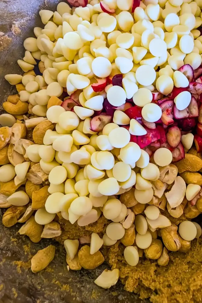 adding white chocolate chips to cookie dough and extras in mixing bowl