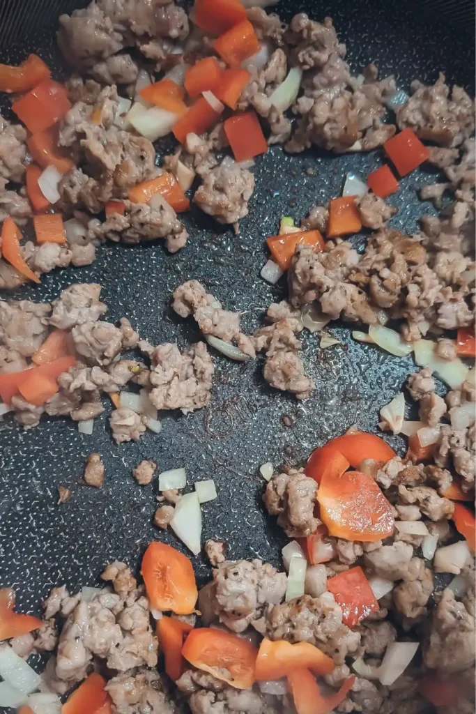 adding onion garlic and red bell pepper to the sausage meat in pan