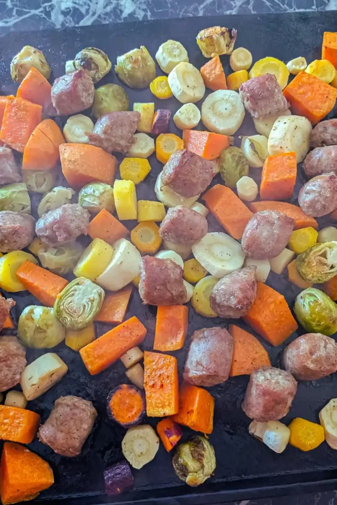 roasted vegetables and cooked Irish bangers on baking sheet