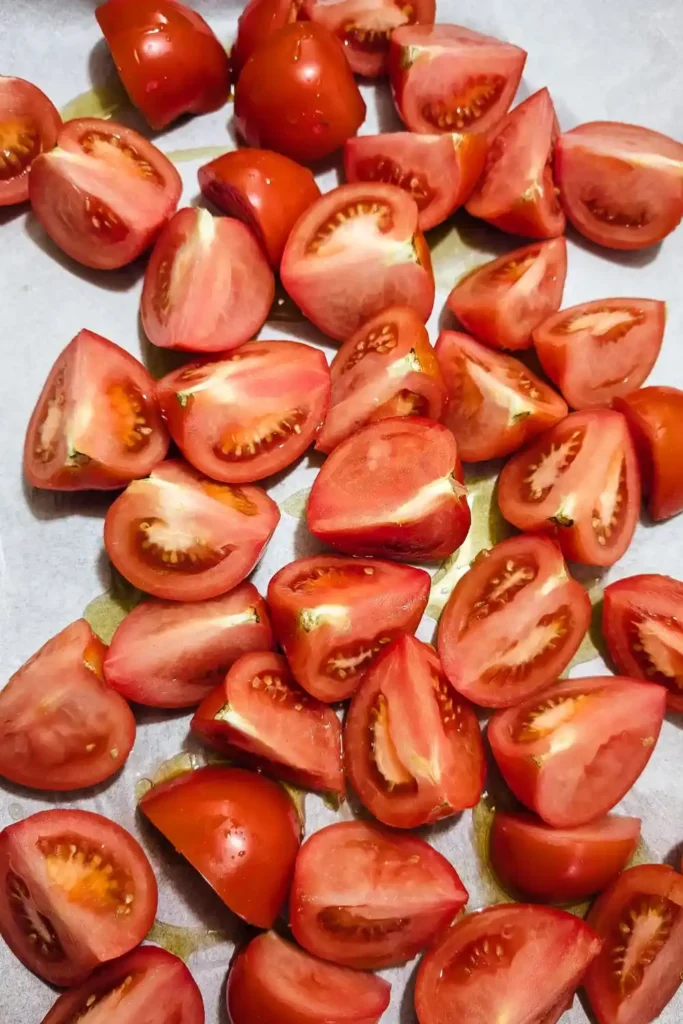 quartered tomatoes with oil on parchment paper on roasting pan