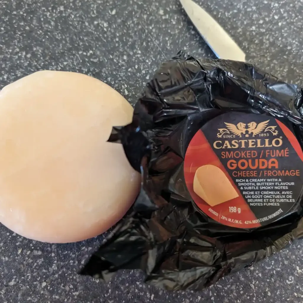 Castello smoked gouda unwrapped on cutting board with knife and wrapper