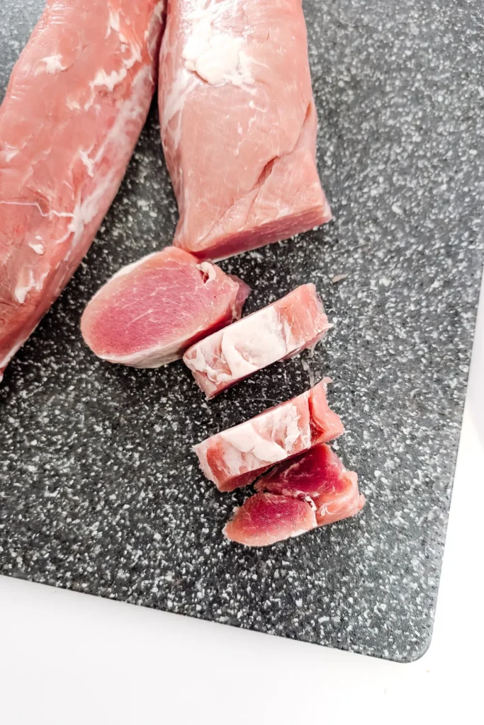 two pork tenderloins being sliced on gray speckled cutting board