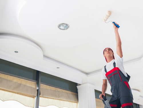 A contractor from Chupps Interior Construction paints a fresh ceiling in a newly finished, bright room.