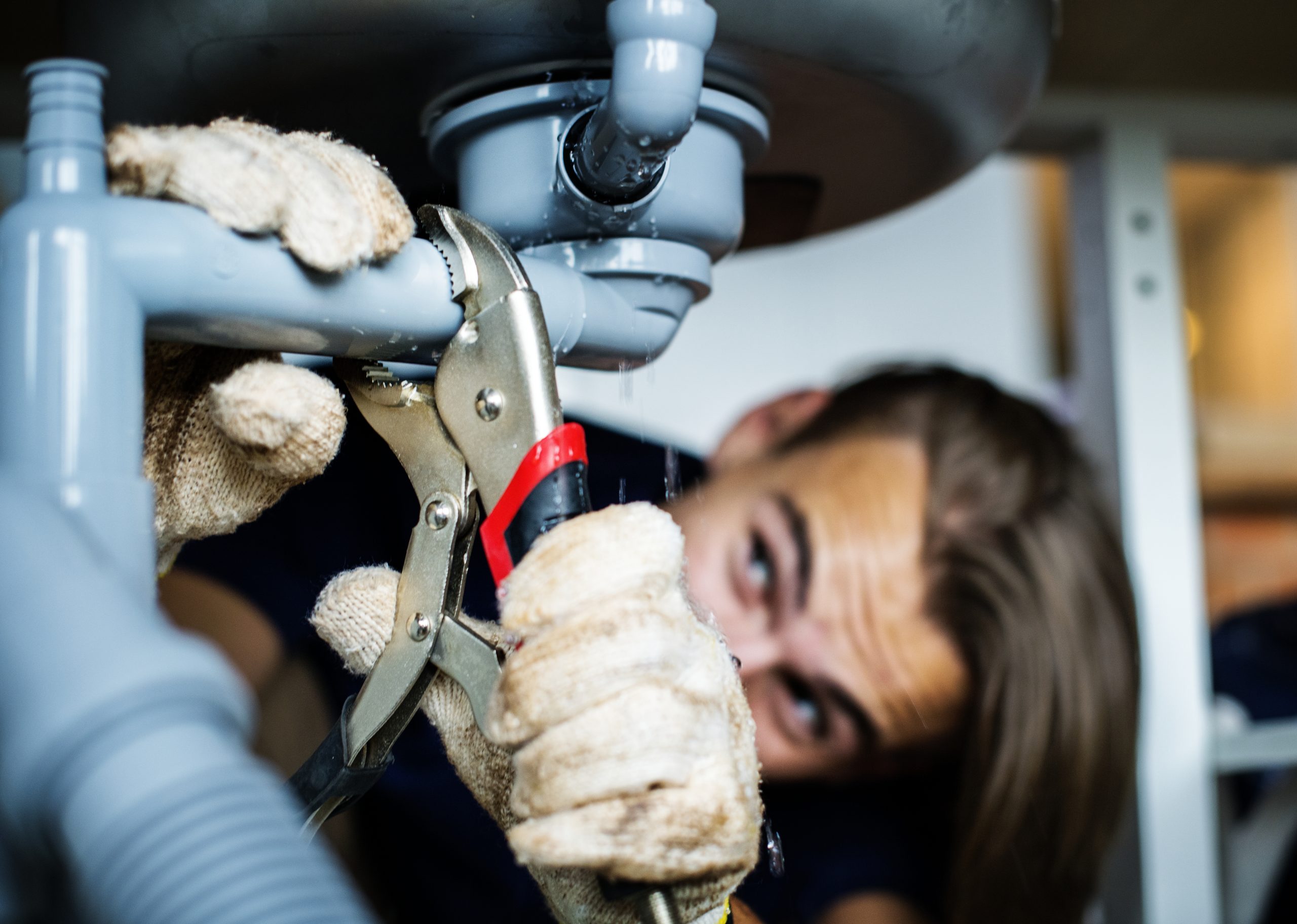 A plumber is fixing pipes under a sink to help water flow properly.