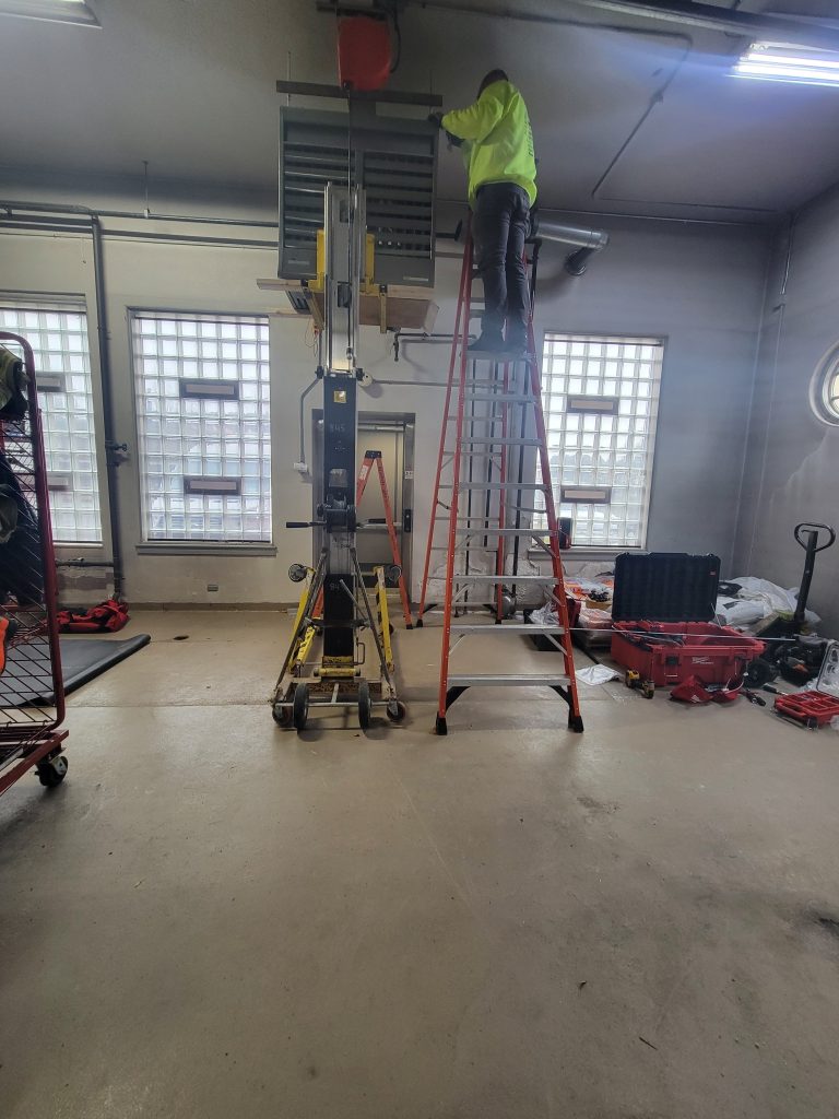 A worker from JP Heating & Cooling repairs or replaces a furnace in a busy garage, making sure everything works safely.