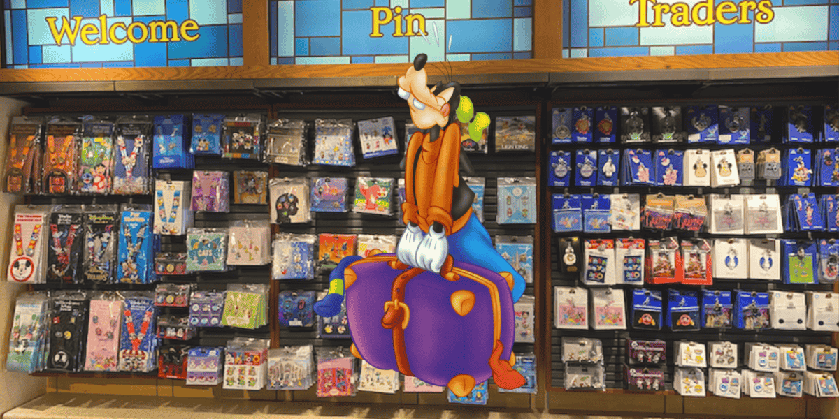 Goofy sitting on a large, colorful pin in front of a wall filled with various collectible pins. The wall has sections labeled "Welcome," "Pin," and "Traders," showcasing a diverse collection.