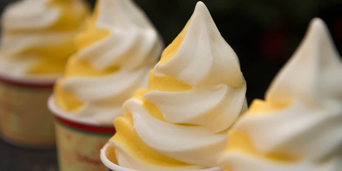 Swirls of vanilla and mango ice cream in cups, reminiscent of Disney World ice cream treats, arranged in a row. The ice cream has a smooth, creamy texture with distinct layers of yellow and white. The background is softly blurred.