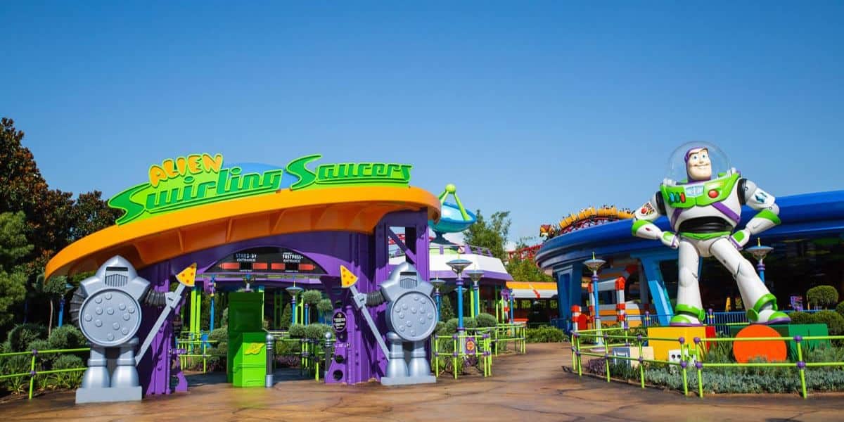 Entrance to the "Alien Swirling Saucers" ride at a theme park, featuring colorful structures and a large statue of a space ranger character. Bright signage and playful design elements create a whimsical atmosphere.