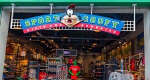 A colorful store entrance featuring the sign "Sport Goofy Gifts and Sundries" with a Goofy character head on top. Inside, shelves display various Disney-themed merchandise and clothing.