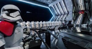 A group of stormtroopers stands in formation inside a futuristic spacecraft. One stormtrooper with a red shoulder pad is in the foreground. A large window shows a view of space with stars and a distant spacecraft.