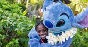 A person is smiling and posing outdoors with a large, plush costumed character resembling Stitch from the animated movie Disney "Lilo & Stitch."