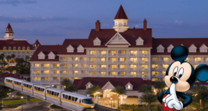 At dusk, a large deluxe hotel with a red roof and white exterior glows with warm lighting. A monorail glides past, embodying the charm of a Disney Resort. In the foreground, an animated character stands thoughtfully with a finger to their mouth.