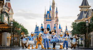 Disney characters, including Mickey and Minnie Mouse, stand in front of Cinderella Castle at Magic Kingdom. They're wearing festive outfits as the castle glows brilliantly. Trees and park buildings line Main Street USA. For a perfect photo tip, capture this enchanting scene just before sunset!.