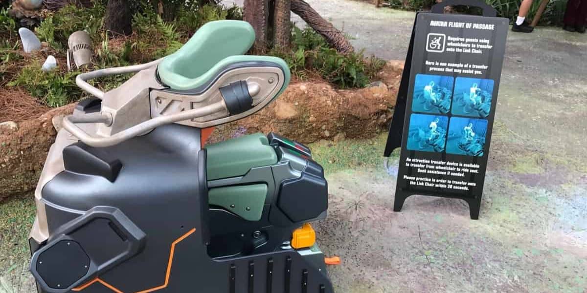 A close-up of a ride vehicle for the Avatar Flight of Passage attraction at Walt Disney World. The bike-like, futuristic design features green and black seats. Beside it, a signage board displays safety instructions and images explaining the ride's seating and restraint system.
