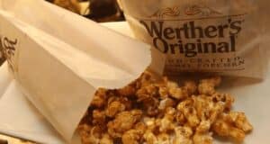 A bag and opened paper pouch of Werther's Original Hand-Crafted Caramel Popcorn delights the senses, with caramel-coated popcorn spilling onto a white tray, reminiscent of the delectable treats found among popcorn snacks at Disney World.