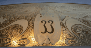 An ornate plaque showcasing the number "33" is embellished with intricate gold and cream swirling designs. The background features detailed leaf-like motifs softly lit, reminiscent of the exclusive allure associated with off-limits locations at Disney Parks.