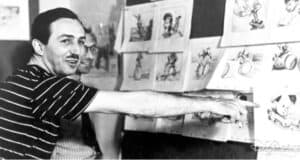 A man gestures animatedly toward storyboard sketches on the wall, immersed in the creative process. Another person is partially visible in the background. The sketches, showcasing cartoon characters in various scenes, offer a glimpse into those eager to learn Disney history through art.