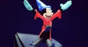A cartoon mouse, reminiscent of the most inspirational Disney characters, wears a blue wizard hat and red robe, standing with arms raised on a rocky ledge against a starry night background.