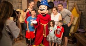 A family poses for a photo with a famous mouse character in a red robe and blue starry hat, inside a themed room with large scrolls. The children look excited, showcasing the magic of taking a toddler to Disney. Ideal memories are made when following tips for toddlers at places like EPCOT.
