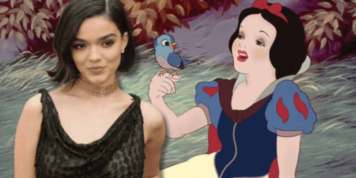 A person in a black dress stands next to an animation of Snow White holding a bluebird. The background features foliage with autumn-colored leaves.
