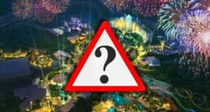 An aerial view of the Epic Universe theme park at night shows it illuminated with various lights and vibrant fireworks in the sky. The park appears bustling with attractions, rides, and green areas. A large warning sign with a question mark is superimposed in the center.