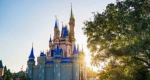 A picturesque view of a fairy tale Cinderella Castle with spires, under a clear blue sky with the sun setting behind, casting a warm glow over the scene at Walt Disney World Resort.