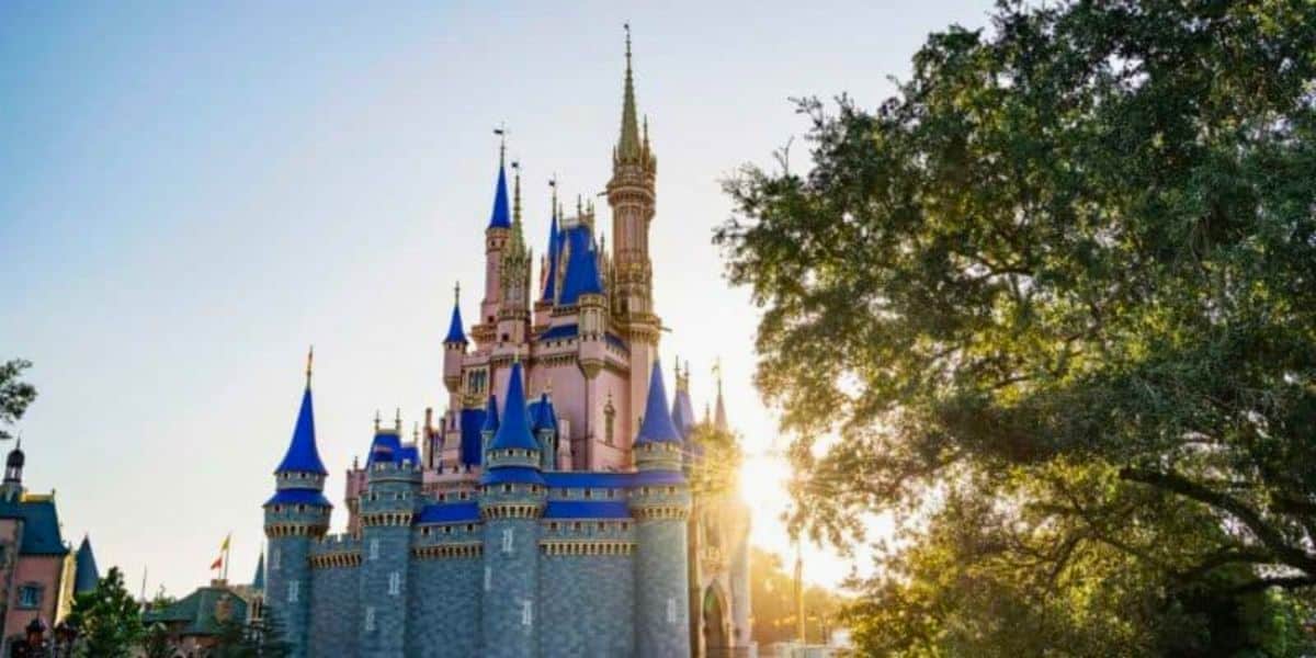 A picturesque view of a fairy tale Cinderella Castle with spires, under a clear blue sky with the sun setting behind, casting a warm glow over the scene at Walt Disney World Resort.
