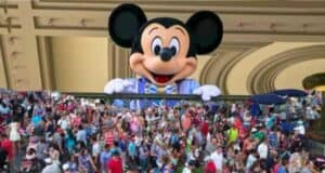 Mickey Mouse, a Disney character, peeking over a ledge above a dense crowd of visitors at a theme park.