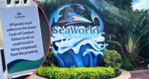 A bright sign at SeaWorld Orlando featuring a large logo of a wave and a tail fin, surrounded by greenery. Inset shows a notice stating all guests must adhere to the Event Code of Conduct or risk being trespassed from the property.