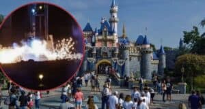 A bustling crowd stands in front of an iconic castle with blue-tiled roofs and towers at Disneyland during daytime. An inset image in the top left corner shows a nighttime scene of fireworks, smoke, and Mickey Mouse, suggesting an event or celebration.