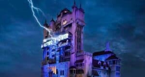 An image of the Tower of Terror, a gloomy, haunted-looking building, illuminated by a neon sign under a stormy sky with a lightning bolt striking.