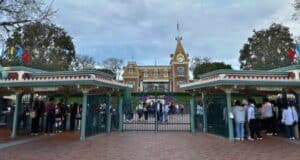 A large crowd of guests in line outside the gates waiting to enter Disneyland Park with the Main Street station of the Disneyland Railroad in the background