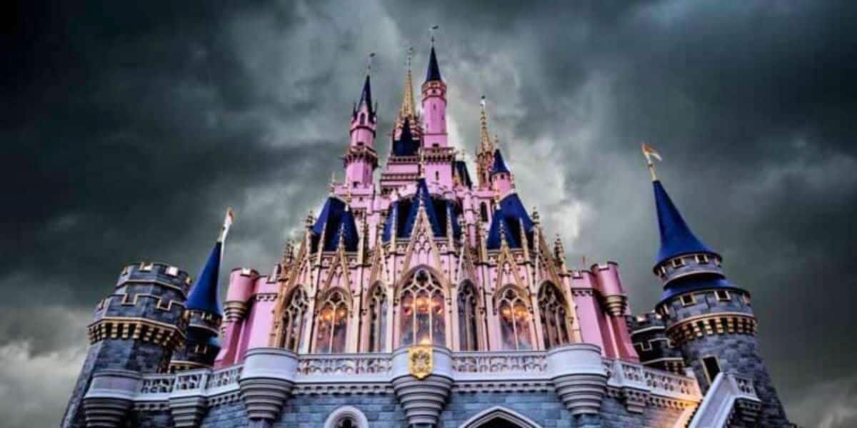 A majestic castle with tall spires and intricate details, illuminated under dramatic dark clouds. The castle is primarily pink with blue rooftops and flags, creating a striking contrast with the stormy sky.