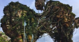 A lush, floating mountain range covered in greenery and vines, with large rocky formations connected by natural bridges. The sky is a mix of clouds and clear areas, creating a mystical atmosphere reminiscent of a fantastical landscape.
