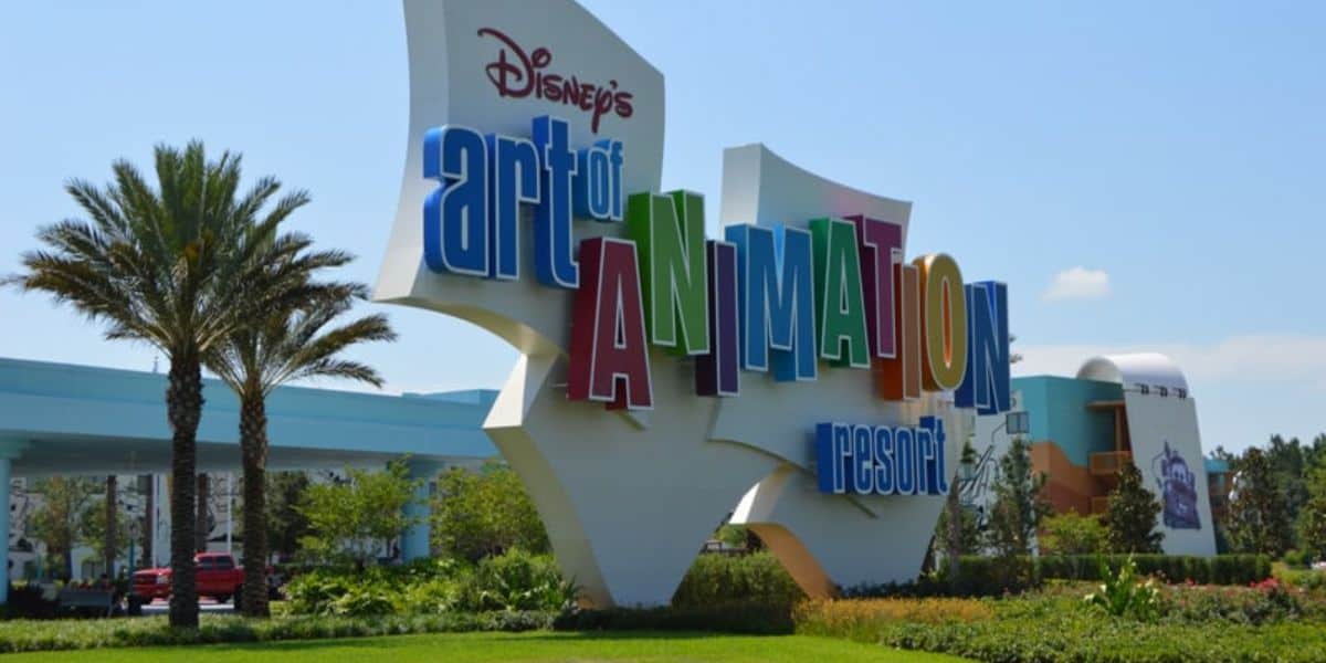 The image shows the colorful entrance sign for Disney's Art of Animation Resort at Walt Disney World. The words "Art of Animation" are prominently displayed in large, multicolored letters, surrounded by lush greenery and palm trees in the background.